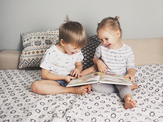 Two kids sitting on bed and reading a book