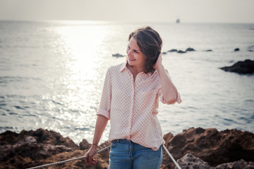 Wall Mural - Beautiful young curly stylish girl in jeans and a pink shirt on the beach, summer and spring portrait, joy and nature