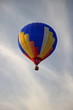 Kolorowy balon unosi się w powietrzu, z podwieszonym koszem, na tle szarobłękitnego nieba