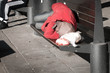 © Srdjan - Poor homeless man sleeps on the wooden bench at the street in the city in red winter jacket, social documentary concept