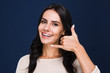 © MARIIA - Just give me a call. Portrait of beautiful young woman looking at camera with smile and gesturing finger phone while standing against black background
