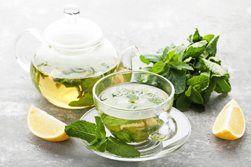 Wall Mural - Cup of tea with mint leafs and lemons on wooden table