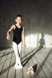 A little adorable young ballerina in black sportwear and white tights doing  stretching in the interior studio posing on camera in bright sunlight from  window Stock Photo