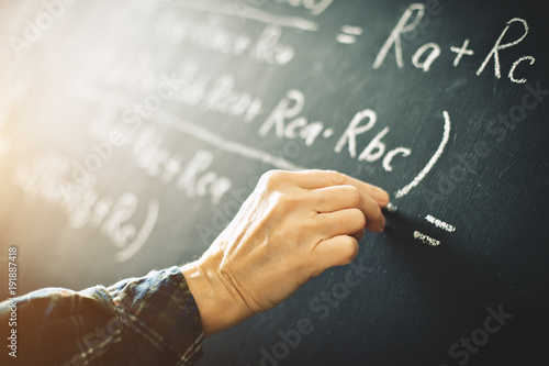 Fotografie, Obraz The teacher writes on a board with chalk a formula for electric current