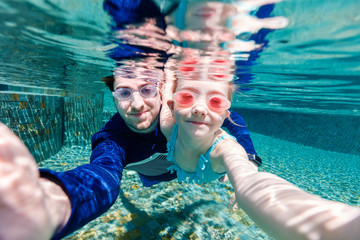 Canvas Print - Father and daughter swimming underwater