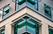 Corner Of A Modern Building With Green Glass, Stone Facade, And Aluminum Awnings.