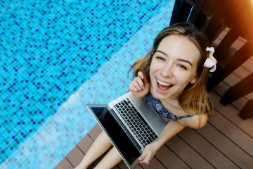 Wall Mural - Female woman smilling looking at camera with laptop on background of pool, picture taken from above. girl is using social networks.