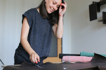 teacher demonstrating future seamstresses how to work with leather, young woman teaching to make bags. Female with red nails wearing grey T-shirt standing near table in workshop and preparing to cut