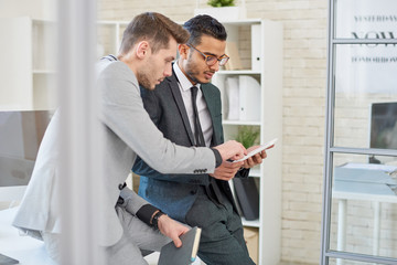 Portrait of successful Middle-Eastern entrepreneur using digital tablet while working with colleague leaning on desk in modern office of startup company