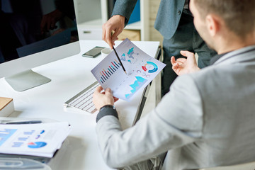 High angle view at two businessmen discussing marketing report at desk while working in modern office