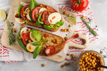 Wall Mural - Caprese sandwich with mozzarella, tomato, fried chickpeas and basil on a wooden board, top view, copy space. Italian cuisine concept.