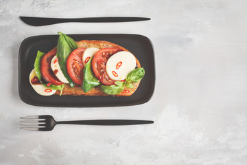 Wall Mural - Caprese sandwich with mozzarella, tomato and basil on a black dish, top view, copy space. Italian cuisine concept.