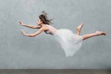 Beautiful Young Woman In Dress Levitating And Looking Away On Grey