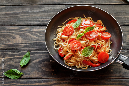 Fotomural Italian pasta with chicken, tomatoes, red pepper,basil in a pan on a wooden tabl