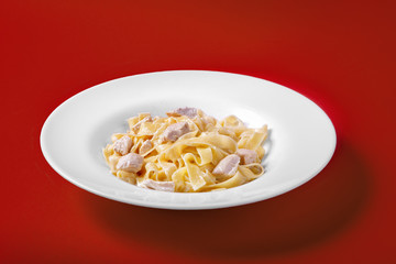 Pasta, noodles with chicken, turkey, decorated with cheese. Monochrome red background. Dish for the menu of the restaurant, bar, cafe. Side view