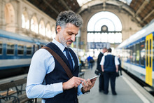 Mature Businessman With Smartphone On A Train Station.
