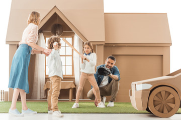 young family playing baseball together on yard of cardboard house isolated on white