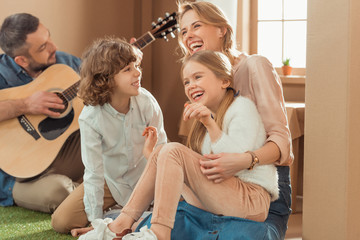 Wall Mural - man playing guitar for his happy family at new cardboard house