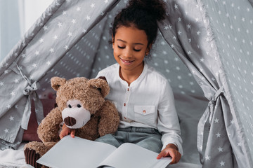 Wall Mural - african american kid reading book and hugging teddy bear