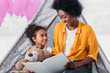 © LIGHTFIELD STUDIOS - happy african american mother and daughter reading book together at home