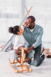 © LIGHTFIELD STUDIOS - african american father and daughter having fun and playing with rocking horse at home