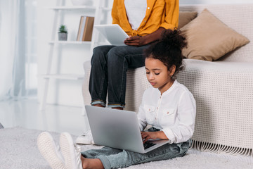 Wall Mural - cropped image of african american mother and daughter using tablet and laptop