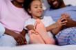 © LIGHTFIELD STUDIOS - african american parents and daughter lying on bed with feet on foreground