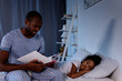 © LIGHTFIELD STUDIOS - african american father reading book for sleeping daughter at home