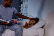 © LIGHTFIELD STUDIOS - african american father holding book and palming sleeping daughter at home