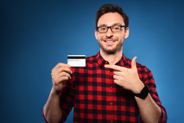 Handsome bearded man in red shirt and  glasses holding a credit card, he is happy winner with million dollars in his bank account