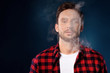 © Антон Зимин - Handsome bearded man smoking electronic vape cigarette, Guy in a red t shirt smoking vapor, Man exhaled vapor on a dark studio background. Man smoking e-cigarette