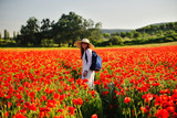 Fototapeta Kuchnia - Young pretty woman in a hat in a flowering poppy field experiences positive emotions
