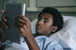 © FS Productions/Blend Images - Black boy laying in hospital bed listening to digital tablet