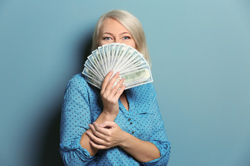 Happy mature woman with lot of dollar banknotes on color background