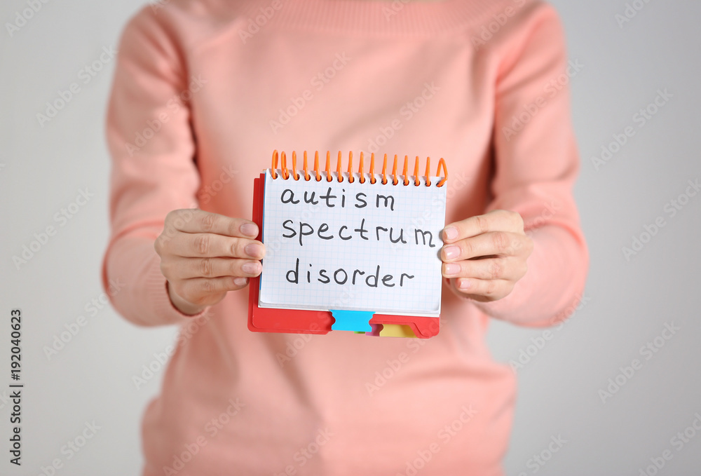 Woman holding notebook with phrase "Autism spectrum disorder" on light background