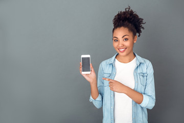 Wall Mural - Young african woman isolated on grey wall studio casual daily lifestyle holding smartphone