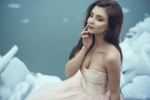 Portrait Of A Young Beautiful Smiling Model In Luxurious Strapless Corset Ball Gown Sitting On Slabs Of Broken Ice At The Misty Seaside With Closed Eyes, Her Hand At Her Lips. Copy Space