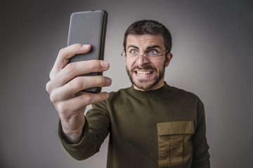 Wall Mural - Young man angry and furious with his cell phone, shouting and yelling in shock