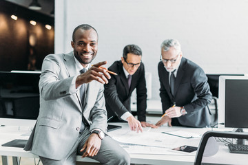 Wall Mural - smiling african american businessman pointing away while business colleagues discussing work in office