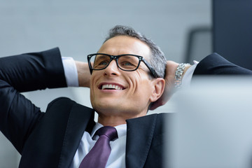 Wall Mural - portrait of cheerful businessman in eyeglasses with hands behind head