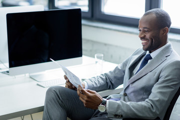 Wall Mural - smiling african american businessman reading newspaper at workplace