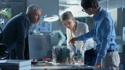 Wall Mural - team of computer engineers lean on the desk and choose printed circuit boards to work with, computer