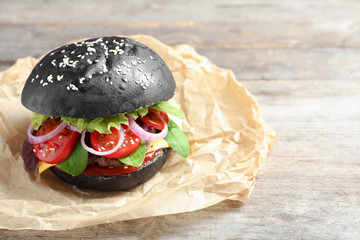 Wall Mural - Tasty burger with black bun on wooden table