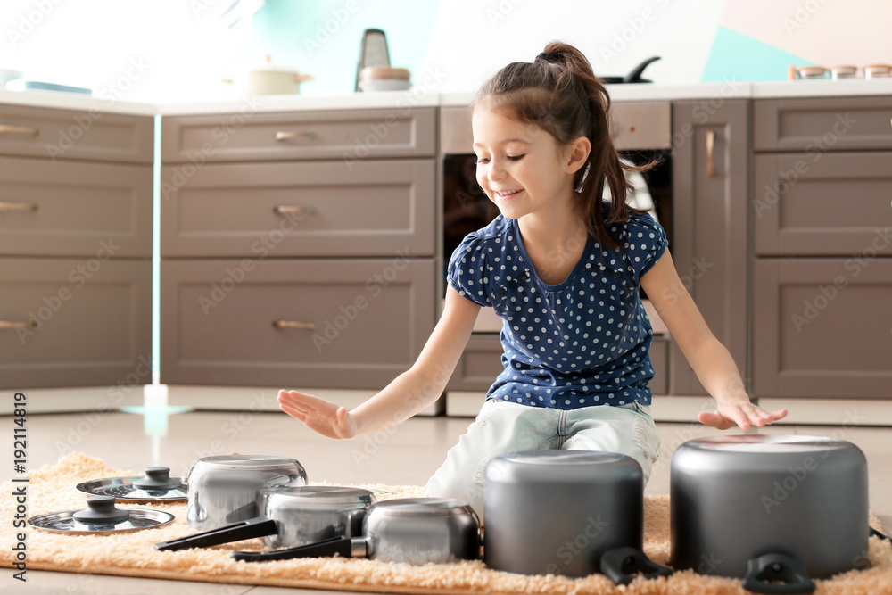 Cute little girl playing with kitchenware as drums in kitchen