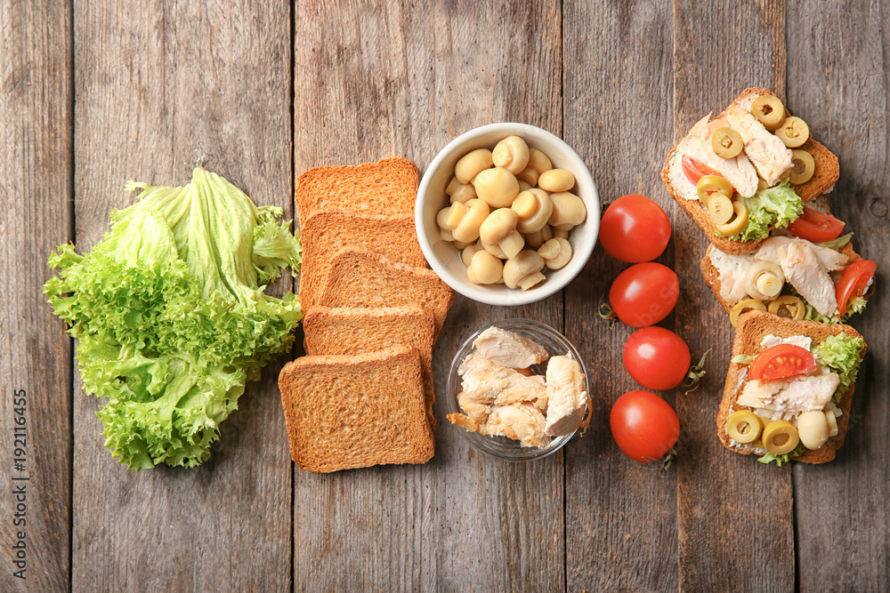 Tasty chicken bruschettas and ingredients on wooden table, flat lay