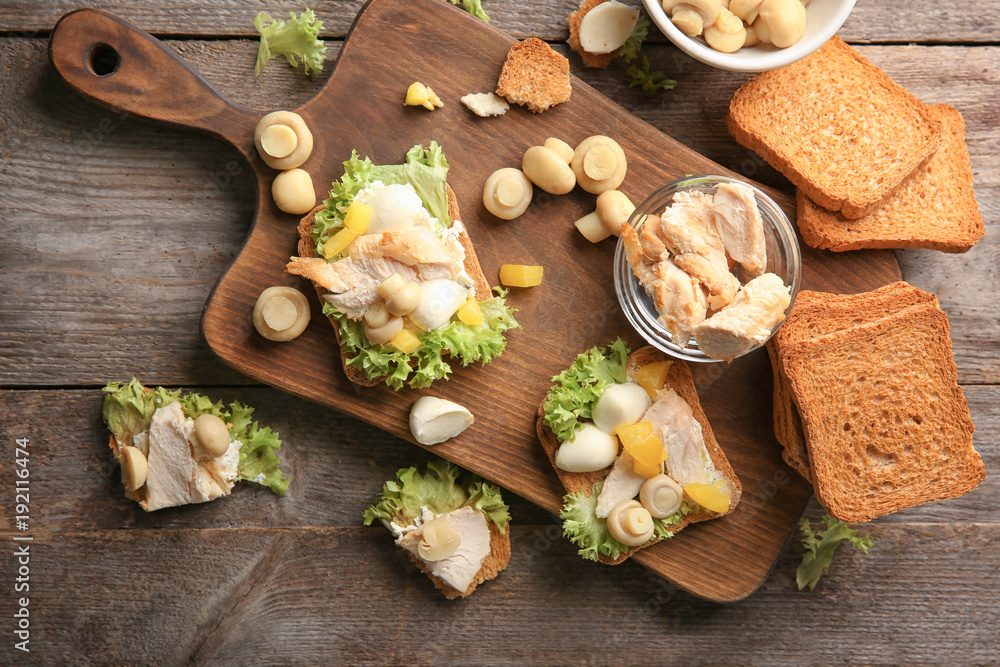 Wooden board with tasty chicken bruschettas on table