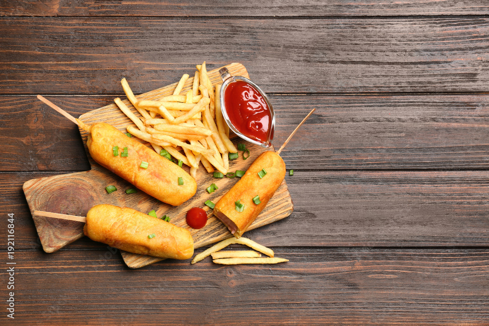 Tasty corn dogs with ketchup on wooden board