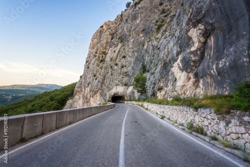 Plakat Wąska, kręta górska droga przez skałę z ciasnym tunelem, serpentynowa asfaltowa droga samochodowa z autostrady do wybrzeża morskiego w Dalmacji, Chorwacja