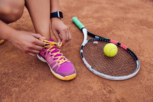 Athlete Woman Getting Ready For Playing A Game Of Tennis, Tying Shoelaces. Close-up View Of Racket And Ball.