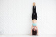Young brunette woman doing a handstand over a white wall
